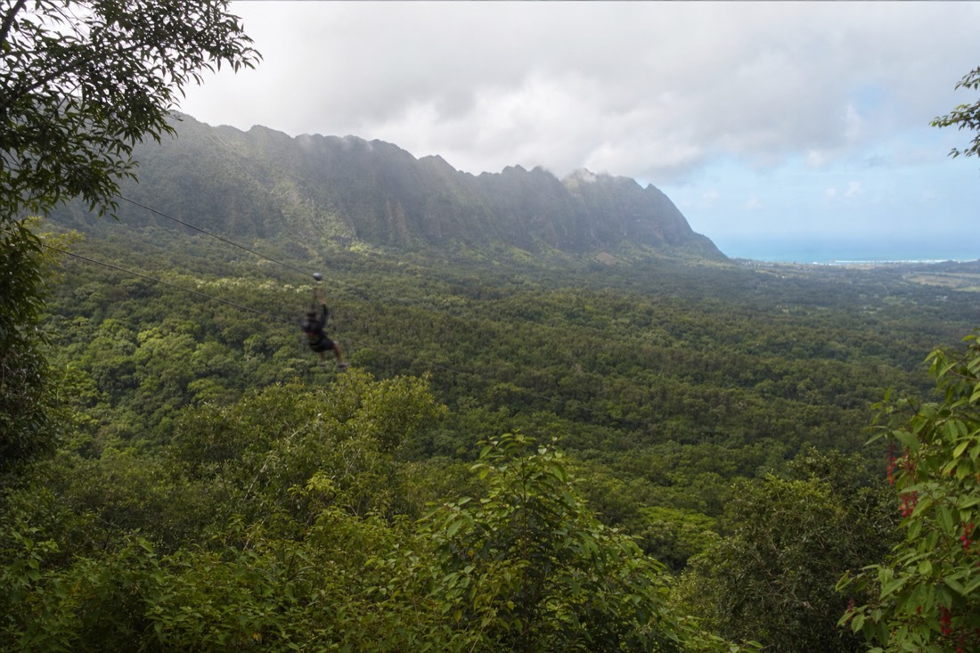 A zipline rider crossing a green jungle valley on a Koloa zipline tour on Kauai's south side