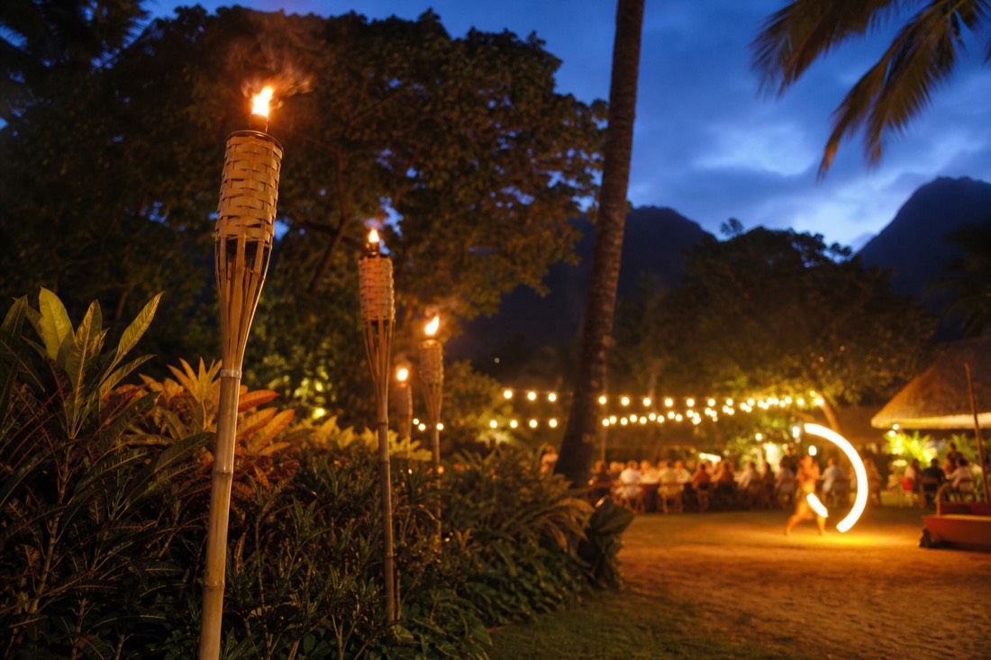 Tiki torches and a fire dancer silhouette at a Kauai luau at dusk