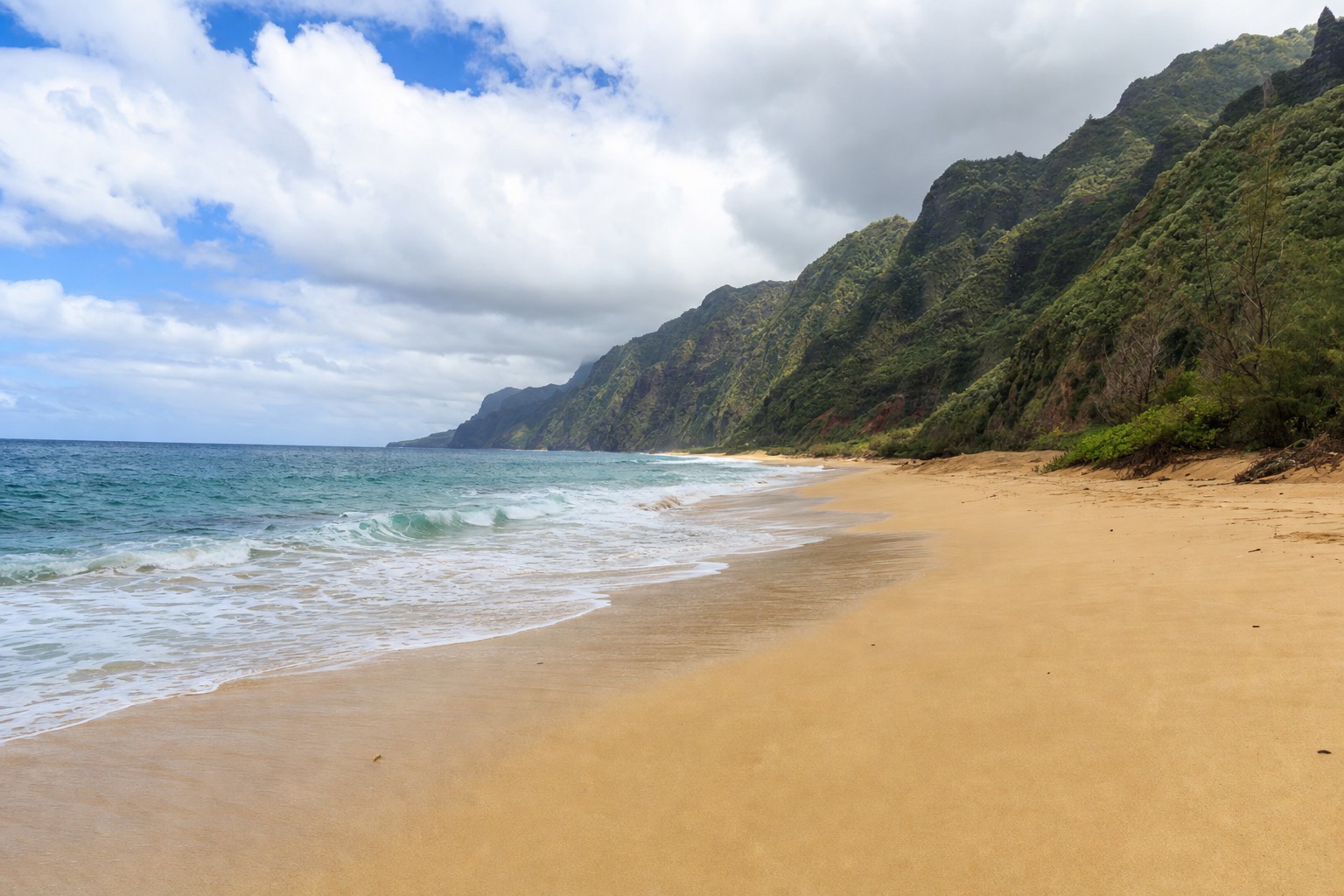 Long empty golden sand at Secret Beach on Kauai's north shore with sea cliffs behind